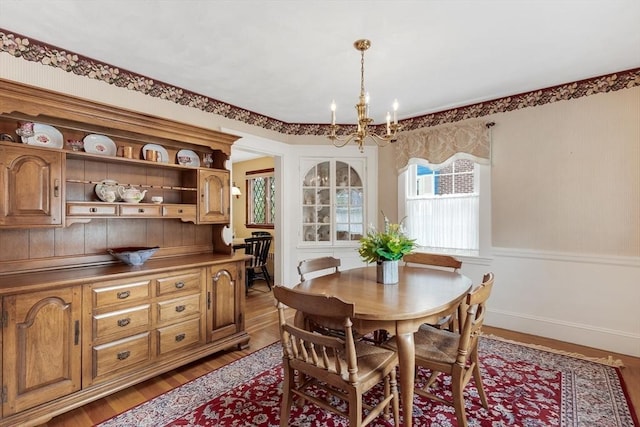 dining area with a chandelier, light wood finished floors, and wainscoting
