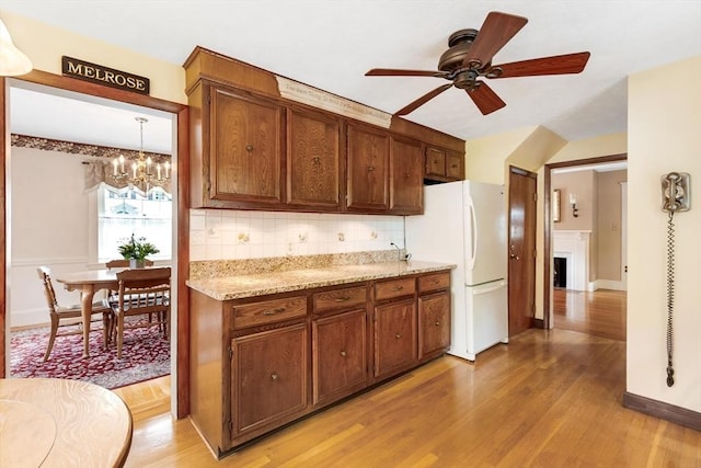 kitchen featuring freestanding refrigerator, backsplash, a ceiling fan, light wood-type flooring, and a chandelier