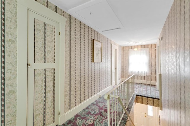hall with wallpapered walls, attic access, and an upstairs landing