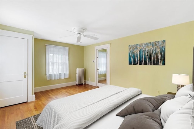 bedroom featuring radiator, baseboards, light wood-style flooring, and a ceiling fan