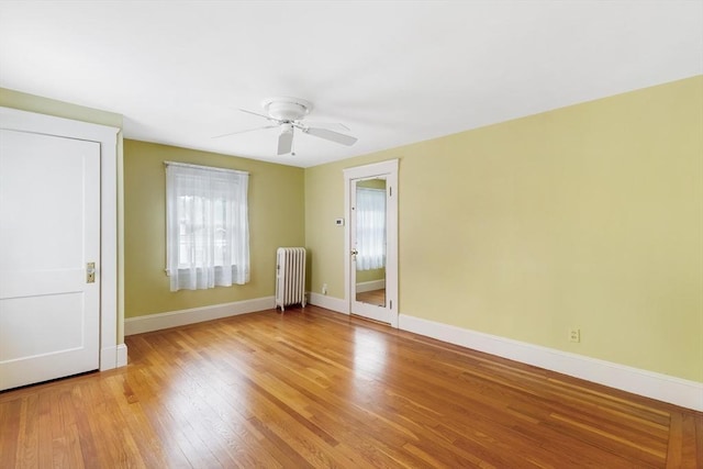 empty room featuring radiator heating unit, ceiling fan, baseboards, and light wood-type flooring