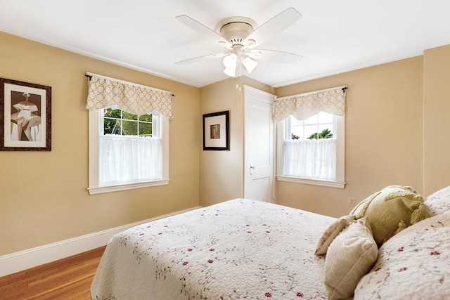 bedroom featuring multiple windows, wood finished floors, baseboards, and ceiling fan