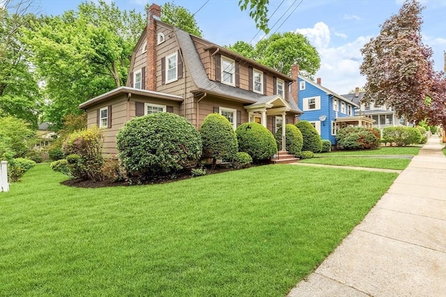 view of front of house with a front lawn, a chimney, a gambrel roof, and roof with shingles
