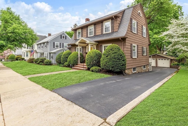 view of front of property featuring an outbuilding, a detached garage, a chimney, a gambrel roof, and a front yard