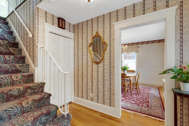 stairway featuring wallpapered walls, wood finished floors, baseboards, and a chandelier