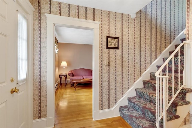 stairs with wood finished floors, wallpapered walls, baseboard heating, and baseboards