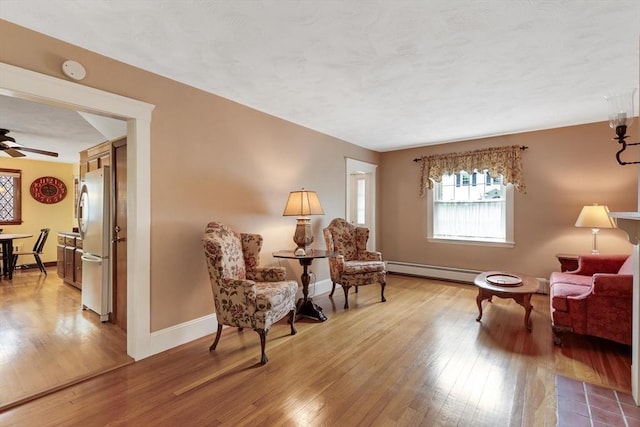 living area with a baseboard radiator, light wood-style floors, baseboards, and a ceiling fan
