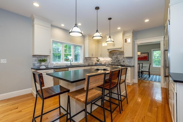 11 Liberty Ave, Burlington, MA 01803 - kitchen with dark countertops, a sink, white cabinets, a breakfast bar, and light wood-style flooring