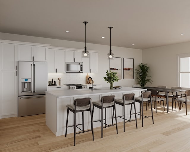 kitchen with light wood-type flooring, stainless steel appliances, decorative light fixtures, and an island with sink