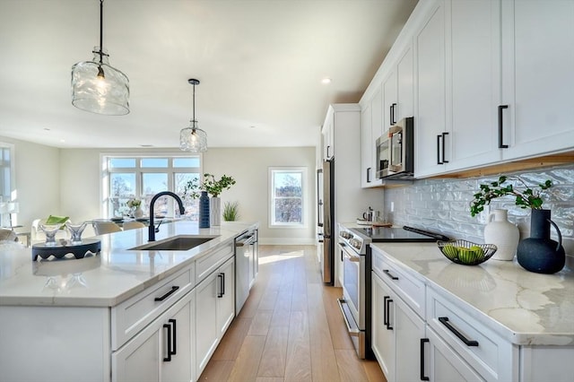 kitchen featuring white cabinetry, a center island with sink, appliances with stainless steel finishes, hanging light fixtures, and sink