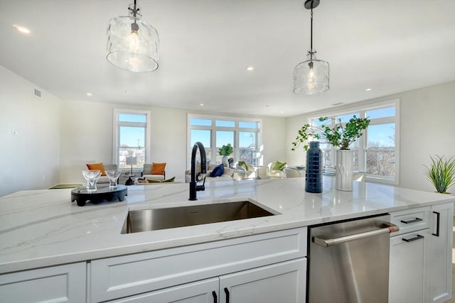 kitchen featuring stainless steel dishwasher, sink, white cabinetry, hanging light fixtures, and light stone counters