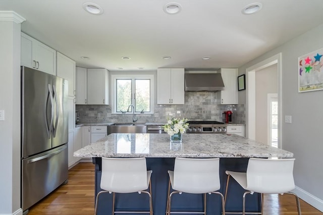 kitchen featuring a sink, a kitchen breakfast bar, wall chimney exhaust hood, stainless steel appliances, and decorative backsplash