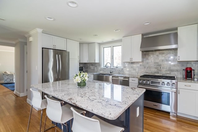 kitchen featuring wall chimney range hood, stainless steel appliances, a sink, and a kitchen bar