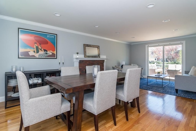 dining space with crown molding, recessed lighting, light wood-style flooring, and a fireplace