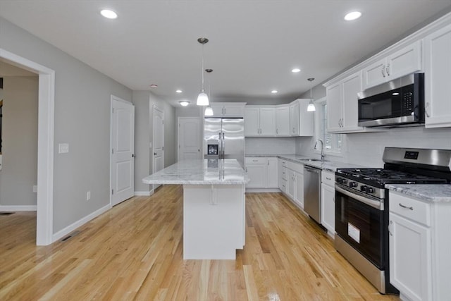 kitchen with white cabinetry, a kitchen island, decorative light fixtures, and appliances with stainless steel finishes