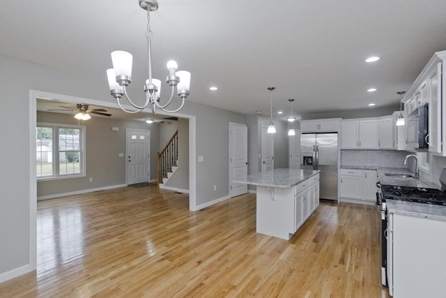 kitchen with ceiling fan with notable chandelier, decorative light fixtures, a kitchen island, white cabinetry, and stainless steel appliances