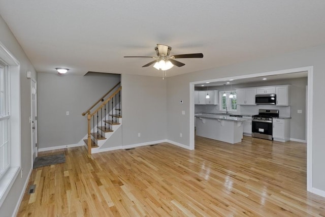 unfurnished living room with ceiling fan, light wood-type flooring, and sink