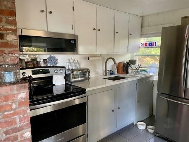 kitchen with appliances with stainless steel finishes, tile patterned flooring, a sink, and white cabinetry