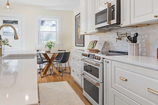 kitchen with white cabinets, hanging light fixtures, light wood-type flooring, and appliances with stainless steel finishes