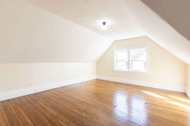 additional living space with hardwood / wood-style flooring, lofted ceiling, and a textured ceiling