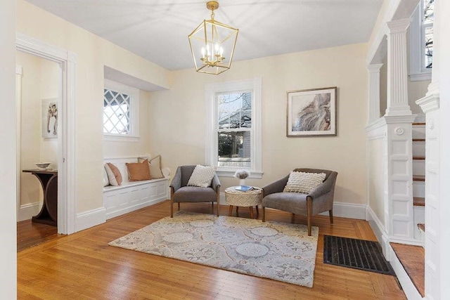 sitting room with ornate columns, wood-type flooring, and an inviting chandelier