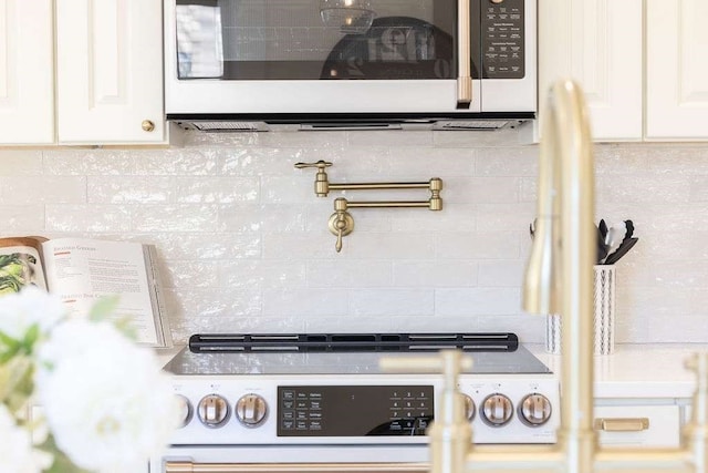 interior details featuring decorative backsplash, white cabinetry, and white stove