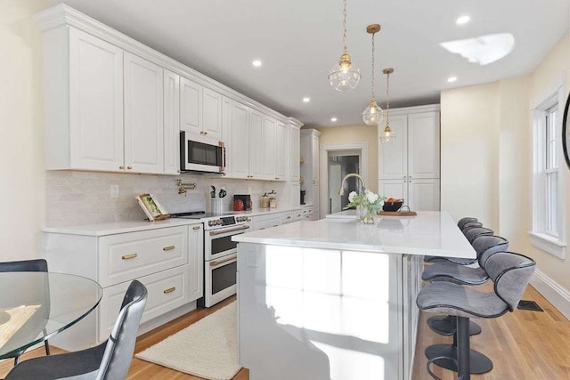 kitchen with decorative light fixtures, white cabinetry, an island with sink, and appliances with stainless steel finishes