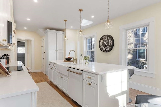 kitchen featuring dishwasher, a center island with sink, white cabinets, hanging light fixtures, and light wood-type flooring