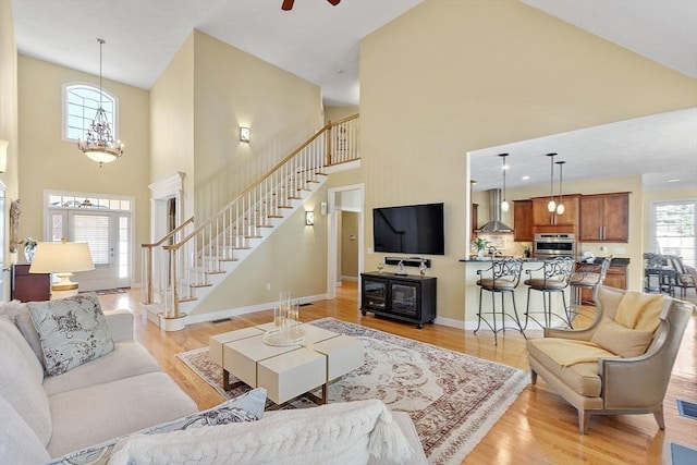 living room featuring a towering ceiling, light hardwood / wood-style floors, ceiling fan with notable chandelier, and plenty of natural light