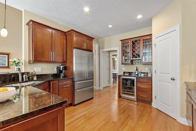 kitchen featuring beverage cooler, light wood-type flooring, pendant lighting, high quality fridge, and sink