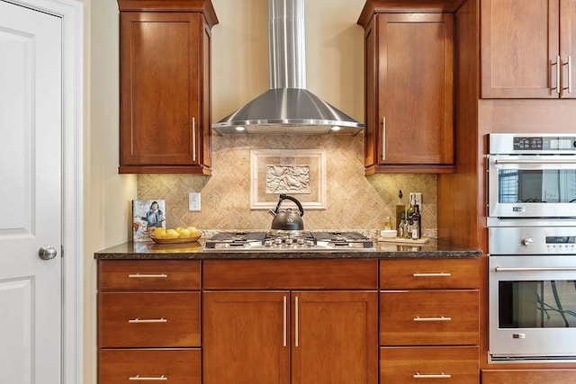 kitchen featuring stainless steel appliances, dark stone counters, wall chimney range hood, and tasteful backsplash