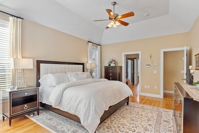 bedroom with ceiling fan, light hardwood / wood-style floors, lofted ceiling, and a tray ceiling