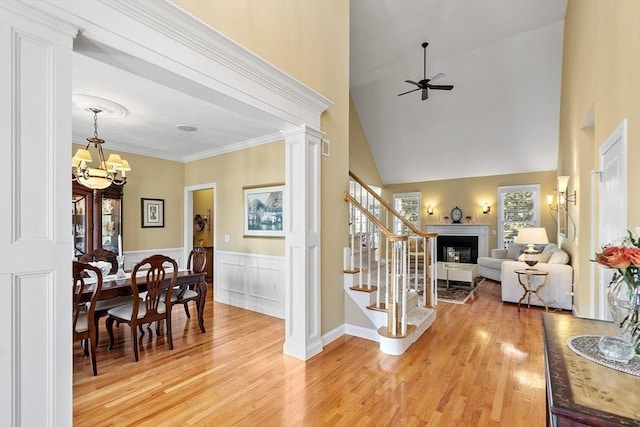 interior space with vaulted ceiling, ornate columns, ornamental molding, light hardwood / wood-style flooring, and ceiling fan with notable chandelier