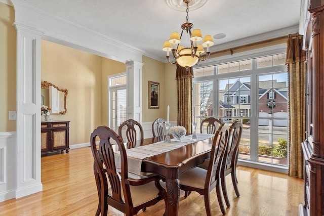 dining space featuring ornate columns, a chandelier, ornamental molding, and light wood-type flooring