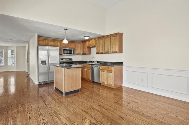 kitchen with a center island, decorative light fixtures, stainless steel appliances, dark countertops, and a sink