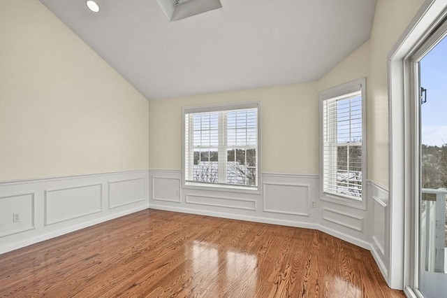 spare room featuring a healthy amount of sunlight, vaulted ceiling, and wood finished floors