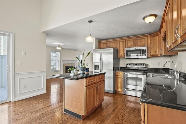 kitchen with stainless steel appliances, a kitchen island, hanging light fixtures, brown cabinetry, and dark countertops