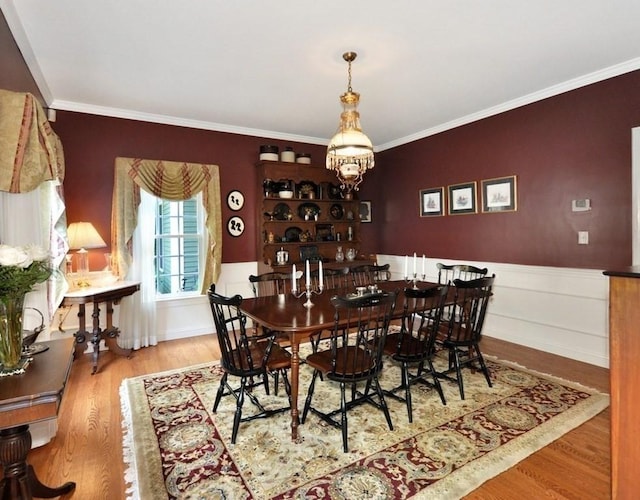 dining area with ornamental molding, wood finished floors, a chandelier, and wainscoting