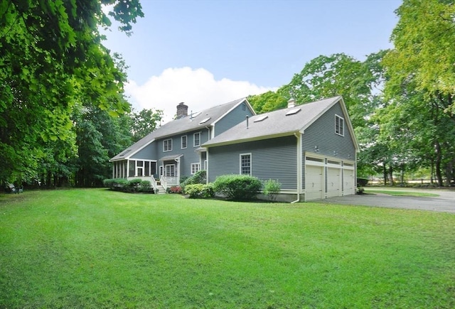 back of house with a lawn, aphalt driveway, an attached garage, a sunroom, and a chimney