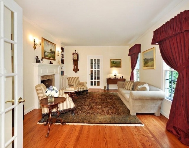 living area featuring a fireplace, wood finished floors, baseboards, and ornamental molding