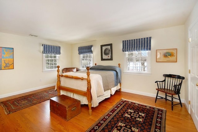 bedroom featuring visible vents, multiple windows, baseboards, and wood finished floors