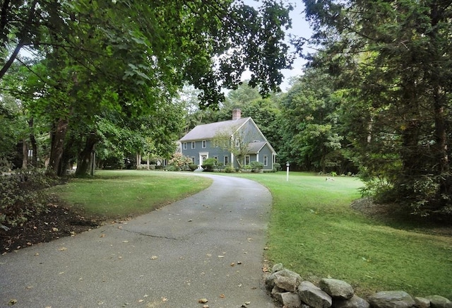 view of front of property featuring driveway, a chimney, and a front yard