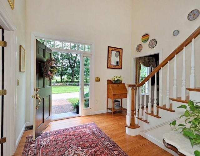 entryway featuring baseboards, light wood-style floors, a high ceiling, and stairs