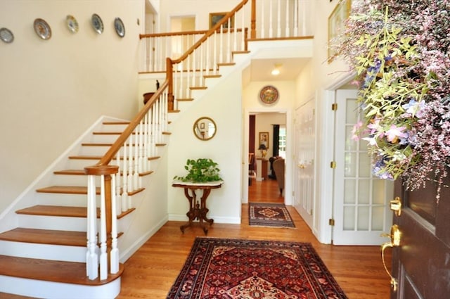 entrance foyer with stairs, baseboards, wood finished floors, and a towering ceiling