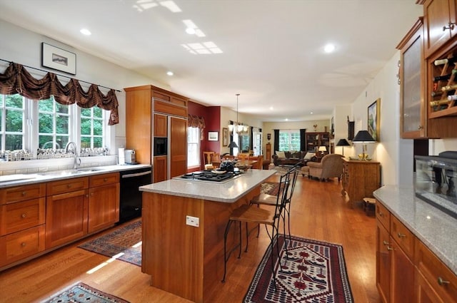 kitchen with brown cabinets, black dishwasher, wood finished floors, a breakfast bar area, and stainless steel gas cooktop