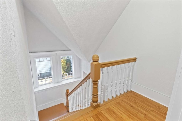 stairway featuring a textured ceiling, vaulted ceiling, and hardwood / wood-style flooring