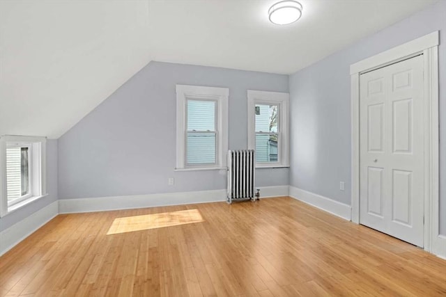 additional living space featuring lofted ceiling, light wood-type flooring, radiator heating unit, and a wealth of natural light