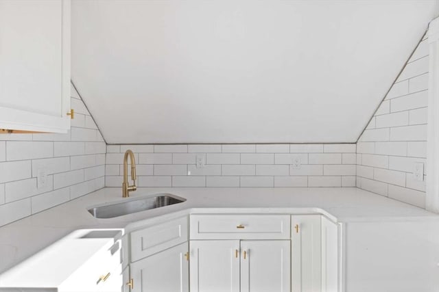 kitchen featuring light stone countertops, white cabinetry, vaulted ceiling, and sink