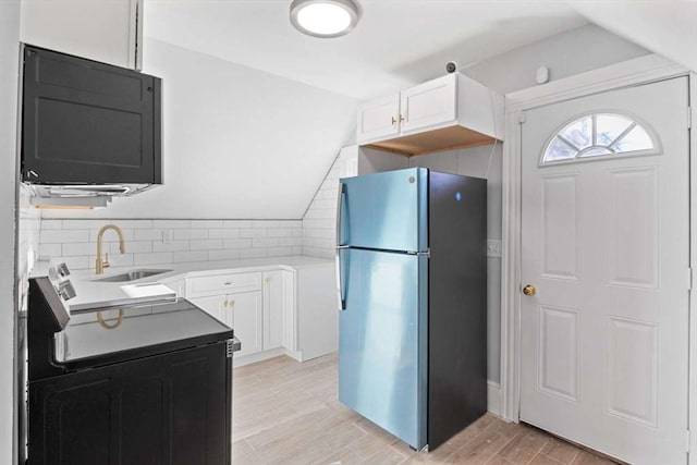 kitchen featuring lofted ceiling, white cabinets, sink, stainless steel fridge, and range