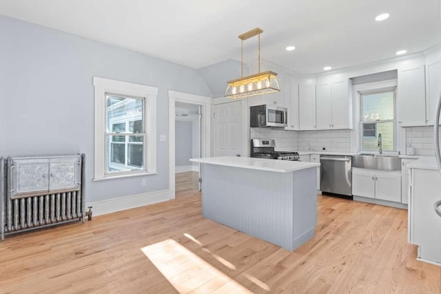 kitchen with pendant lighting, sink, appliances with stainless steel finishes, white cabinetry, and radiator heating unit